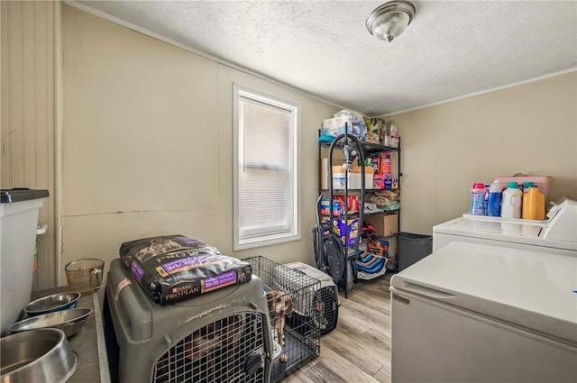 clothes washing area with laundry area, washing machine and dryer, light wood-type flooring, and a textured ceiling