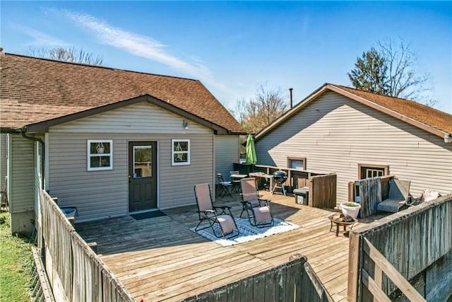 rear view of property with outdoor dining area, roof with shingles, and a wooden deck