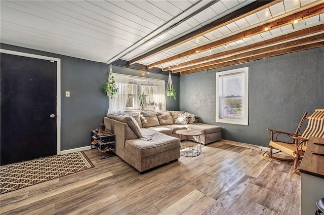 living area featuring wood-type flooring, baseboards, a textured wall, and beamed ceiling