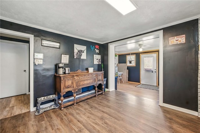 interior space featuring baseboards, ceiling fan, ornamental molding, and wood finished floors