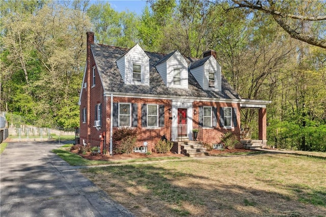 new england style home with brick siding, a chimney, driveway, and a front yard
