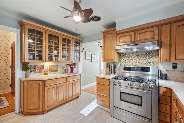 kitchen with baseboards, ceiling fan, stainless steel gas range oven, light countertops, and under cabinet range hood