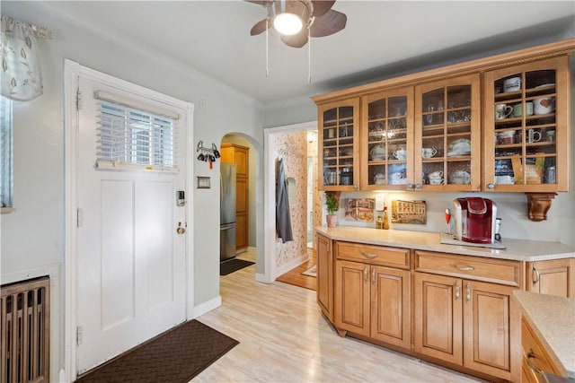 kitchen with a ceiling fan, glass insert cabinets, radiator heating unit, light countertops, and arched walkways
