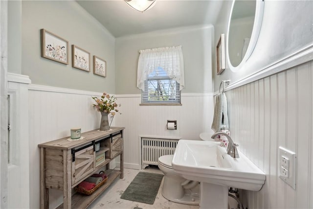 half bathroom with a sink, radiator heating unit, toilet, and a wainscoted wall