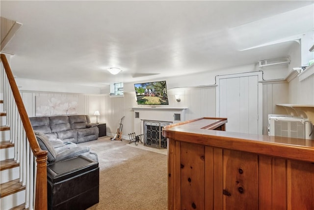 living area featuring a fireplace with flush hearth, carpet flooring, and stairs