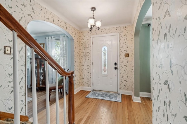 entrance foyer with arched walkways, baseboards, and light wood-type flooring