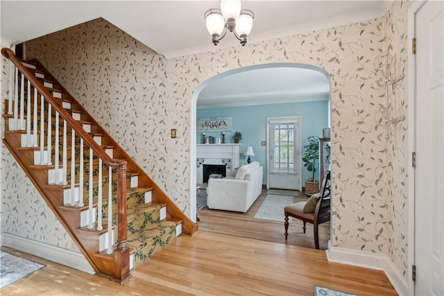 foyer with ornamental molding, wood finished floors, a fireplace, stairway, and arched walkways