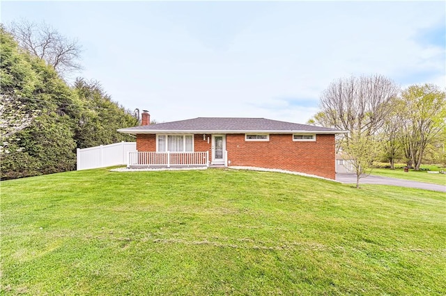 ranch-style house featuring a chimney, a front yard, brick siding, fence, and aphalt driveway
