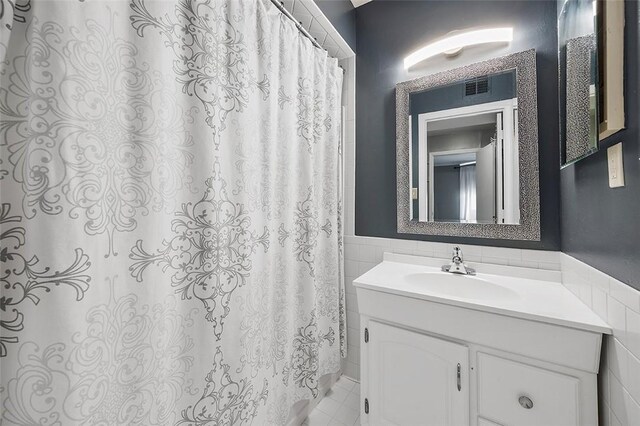 full bathroom featuring tile walls, wainscoting, visible vents, and vanity