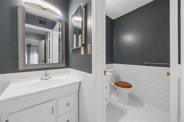 bathroom with visible vents, wainscoting, toilet, tile walls, and tile patterned floors