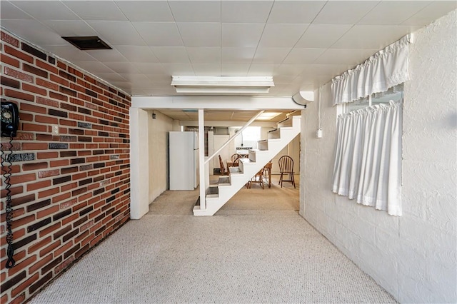 finished basement featuring freestanding refrigerator, stairs, brick wall, and visible vents