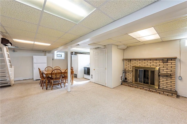 interior space with carpet floors, freestanding refrigerator, a drop ceiling, and a brick fireplace