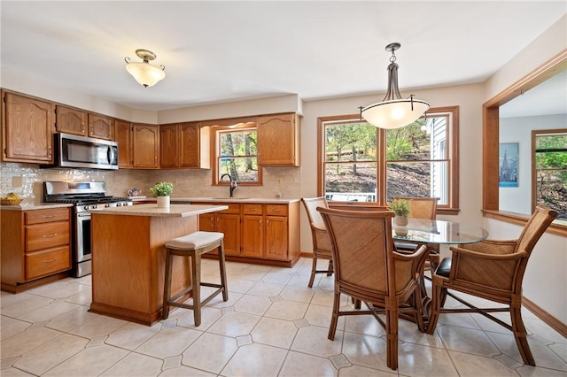 kitchen featuring brown cabinetry, light countertops, tasteful backsplash, a sink, and appliances with stainless steel finishes
