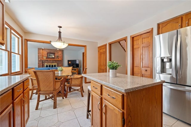 kitchen with light stone counters, stainless steel fridge with ice dispenser, a brick fireplace, a center island, and decorative light fixtures