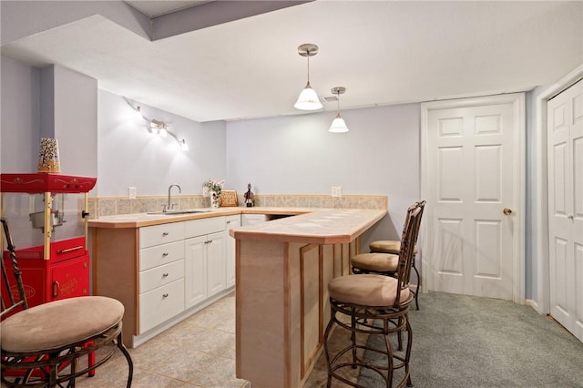 kitchen with hanging light fixtures, a sink, white cabinets, a peninsula, and a breakfast bar