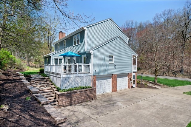 back of property featuring a chimney, a wooden deck, brick siding, concrete driveway, and an attached garage