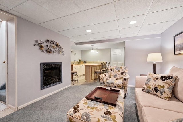 living room with baseboards, light carpet, a drop ceiling, and indoor wet bar