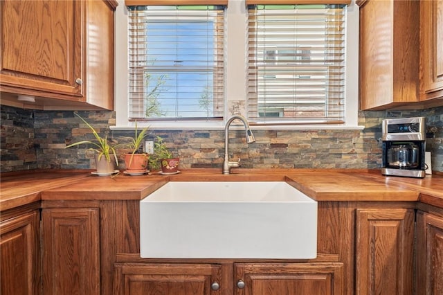 kitchen with a sink, backsplash, brown cabinets, and butcher block countertops