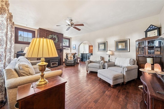living room with arched walkways, a ceiling fan, dark wood-type flooring, and a wealth of natural light