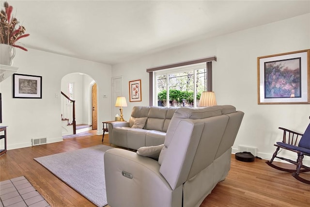 living area featuring arched walkways, baseboards, light wood finished floors, and visible vents