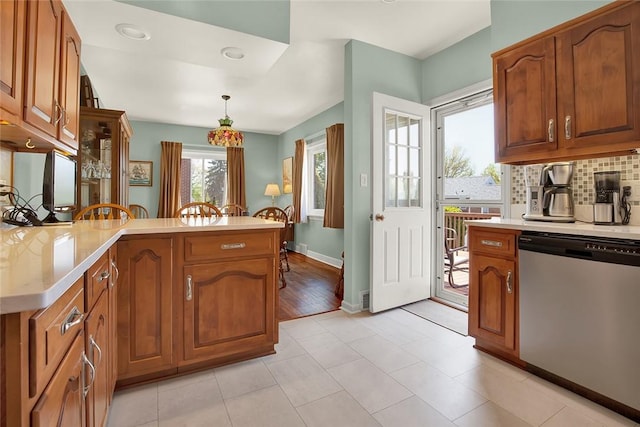 kitchen with light countertops, brown cabinetry, a peninsula, and dishwasher