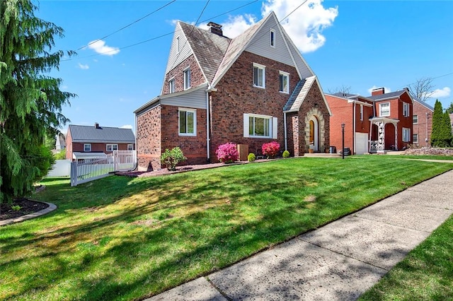 tudor-style house with brick siding, fence, a chimney, and a front yard