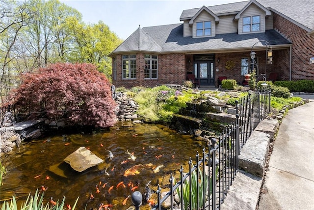 view of front of home with fence, a small pond, roof with shingles, and brick siding