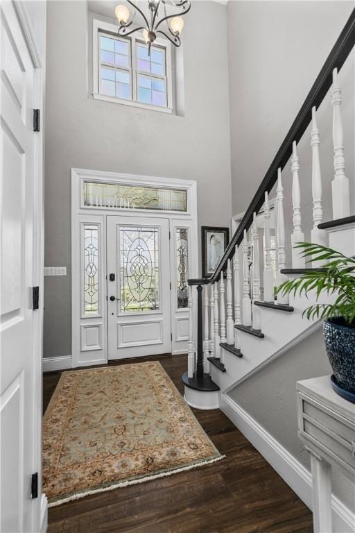 foyer entrance featuring an inviting chandelier, stairs, baseboards, a towering ceiling, and dark wood-style floors