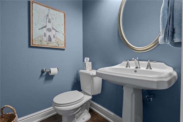 half bathroom featuring baseboards, wood finished floors, and toilet