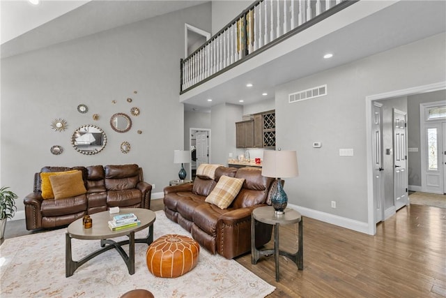 living room with recessed lighting, baseboards, wood finished floors, a towering ceiling, and visible vents