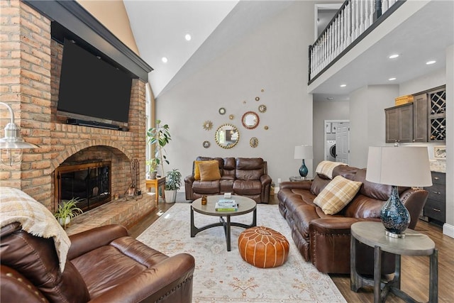 living area featuring washer / clothes dryer, a fireplace, wood finished floors, high vaulted ceiling, and baseboards