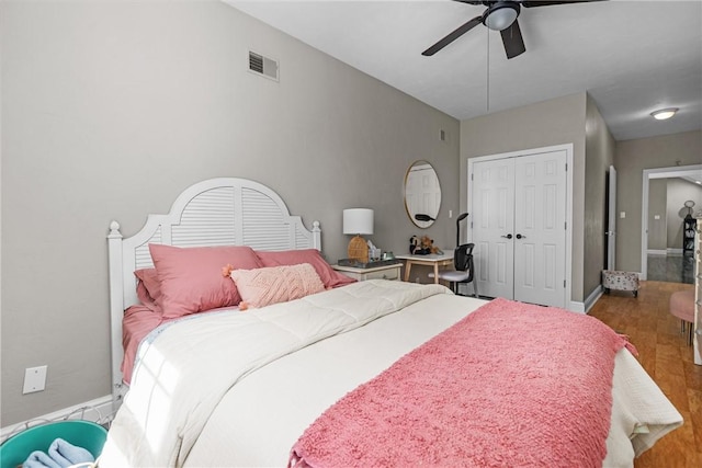 bedroom featuring visible vents, a closet, wood finished floors, baseboards, and a ceiling fan