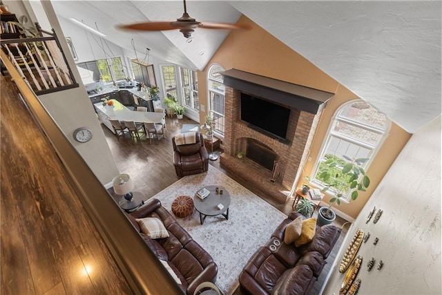living area with high vaulted ceiling, a ceiling fan, wood finished floors, and a brick fireplace