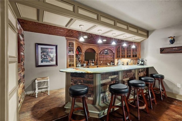 bar featuring indoor wet bar, baseboards, a sink, dark wood finished floors, and decorative light fixtures