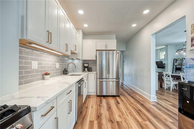 kitchen with appliances with stainless steel finishes, a sink, light wood-style flooring, and light stone counters