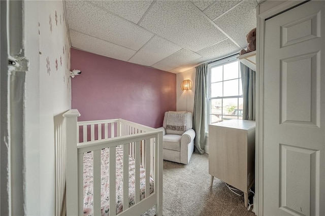 carpeted bedroom with a nursery area and a paneled ceiling