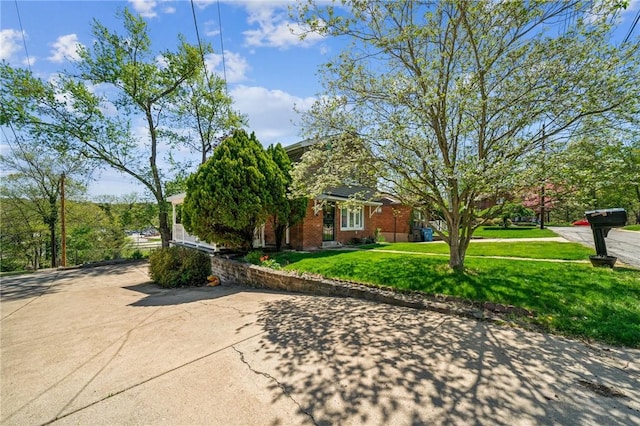 obstructed view of property featuring brick siding, driveway, and a front lawn