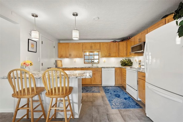 kitchen featuring a breakfast bar area, a textured ceiling, decorative light fixtures, light stone countertops, and white appliances