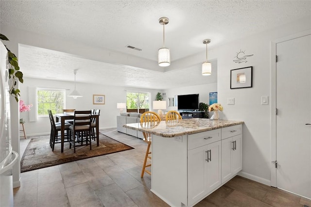 kitchen featuring white cabinetry, a kitchen bar, a textured ceiling, and visible vents