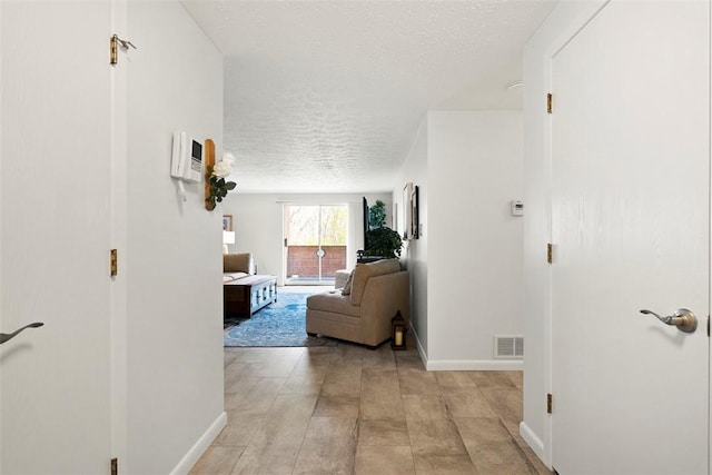 hallway with visible vents, a textured ceiling, and baseboards