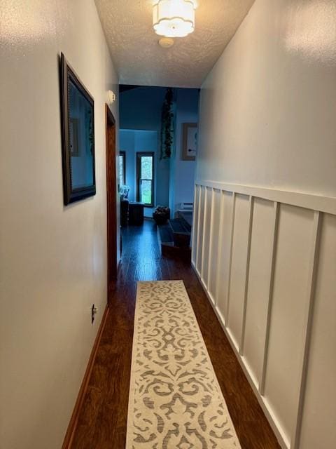 hall featuring baseboards, a textured ceiling, and dark wood finished floors