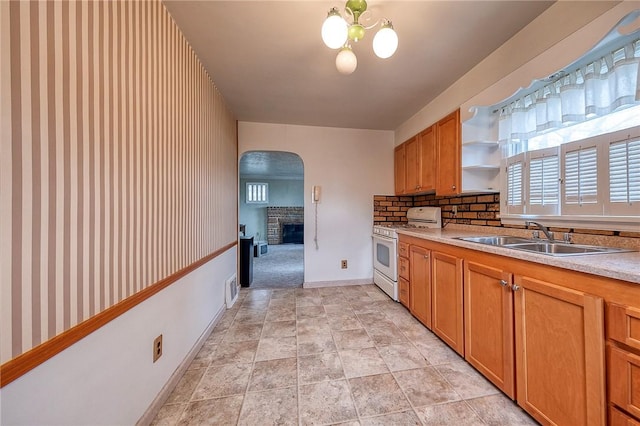 kitchen with a fireplace, white gas stove, light countertops, arched walkways, and a sink