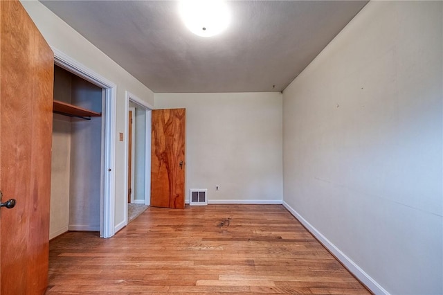 unfurnished bedroom with baseboards, a closet, wood finished floors, and visible vents