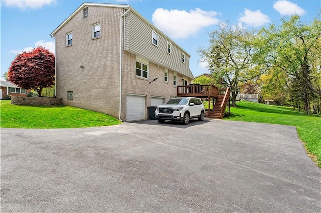view of side of home featuring a lawn, a deck, stairway, brick siding, and aphalt driveway