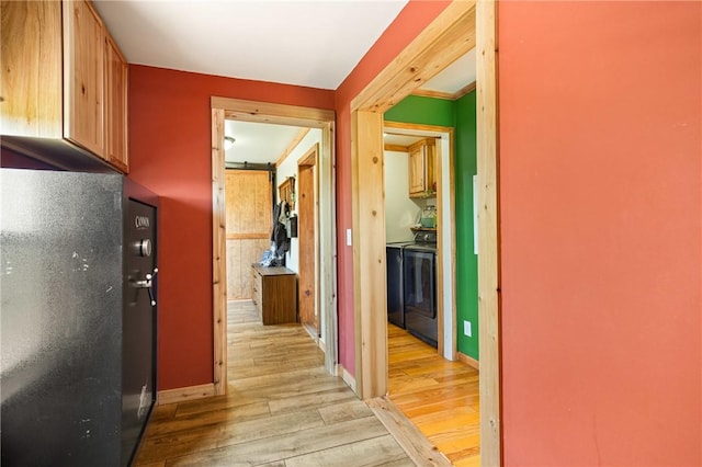 corridor featuring baseboards, washer and clothes dryer, and light wood-style flooring