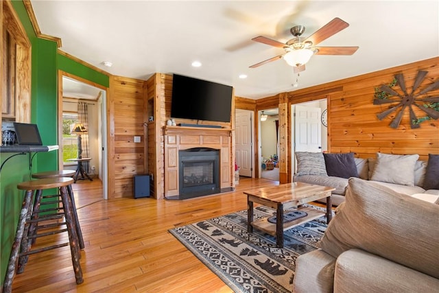 living area featuring wooden walls, recessed lighting, ceiling fan, and a glass covered fireplace