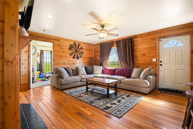 living area with a ceiling fan, wooden walls, and hardwood / wood-style flooring