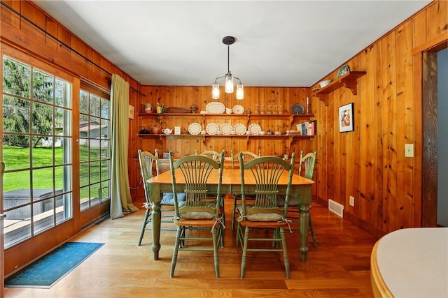dining room with a wealth of natural light, light wood-type flooring, wood walls, and visible vents