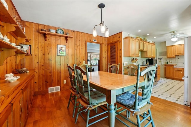 dining space featuring wooden walls, ceiling fan, light wood-type flooring, and visible vents
