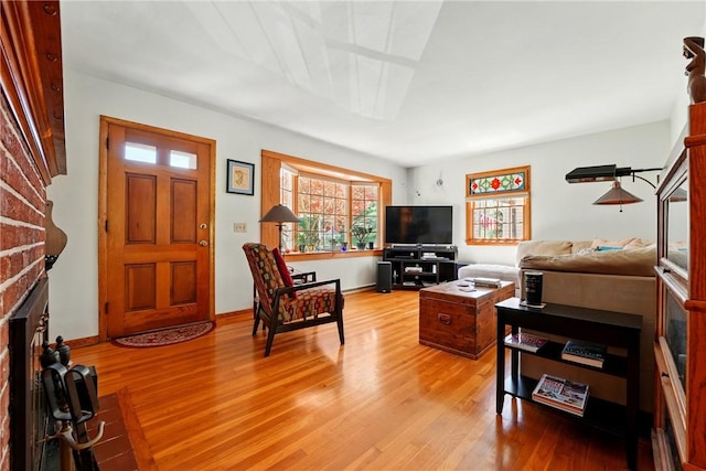 living room with baseboards, a brick fireplace, and light wood-type flooring